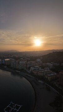 Aerial view of Malaga bullring (Plaza de Toros de la Malagueta) illuminated at sunset. Cinematic drone shot of the coastal arena, Mediterranean sea, and city skyline during golden hour.