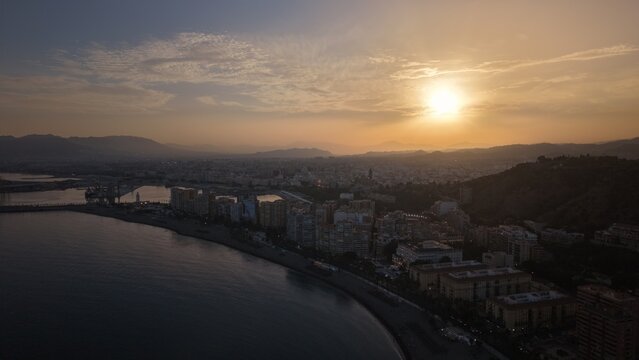 Aerial view of Malaga bullring (Plaza de Toros de la Malagueta) illuminated at sunset. Cinematic drone shot of the coastal arena, Mediterranean sea, and city skyline during golden hour.