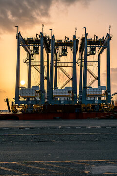 View of the gantry cranes at the Caucedo Logistics Center during sunset, with industrial machinery and paved port area in the foreground in Andres, Santo Domingo, Dominican Republic.