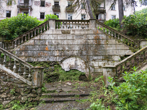 Abandoned stone staircase overgrown with green vegetation in city of Akarmara, Abkhazia. Grand symmetrical steps of a ruined building covered in moss. Historical architecture