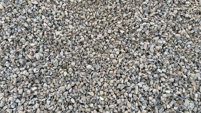 A pile of gravel in various sizes and brownish-gray hues, featuring a rough, natural texture suitable as a background for construction materials or road surfaces.