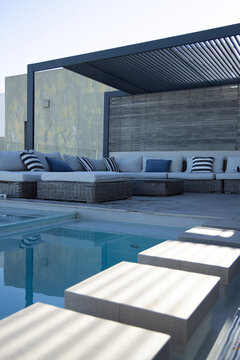 L-shaped rattan sectional is sitting under dark metal pergola by pool, navy pillows reflecting