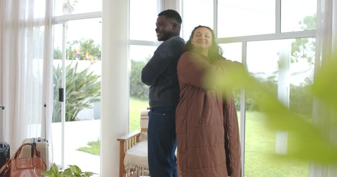 Camera revealing African American couple back-to-back smiling by glass doors with brown puffer coat