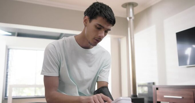 African American man adjusting BP cuff and using monitor on bed, checking health, showing concern