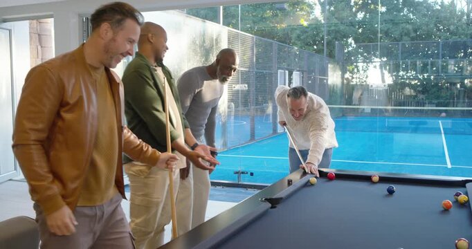 Diverse men deciding shooter, sweatered man stepping and striking to sink ball on home pool table