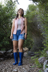 Obraz premium African American woman standing on narrow woodland path wearing blue rubber boots and smartwatch