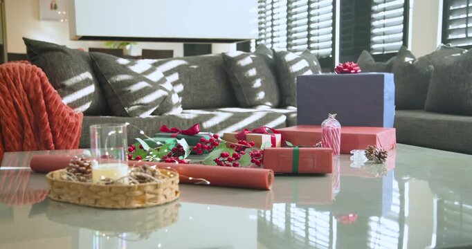 Camera is pulling back, revealing wrapped gifts on table to show sofa while sunlight is shifting