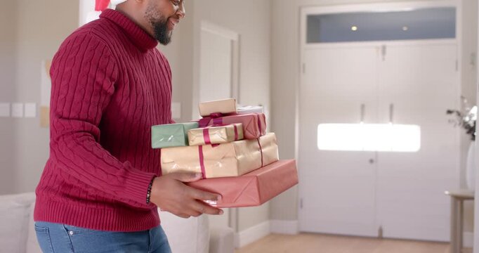 African American family placing gifts under tree at home as man entering carrying holiday presents