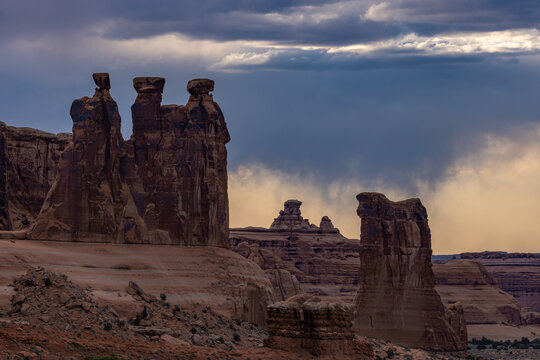 View of the Three Gossips rock formations in Arches National Park under a dramatic stormy sky in Moab, Utah, United States.