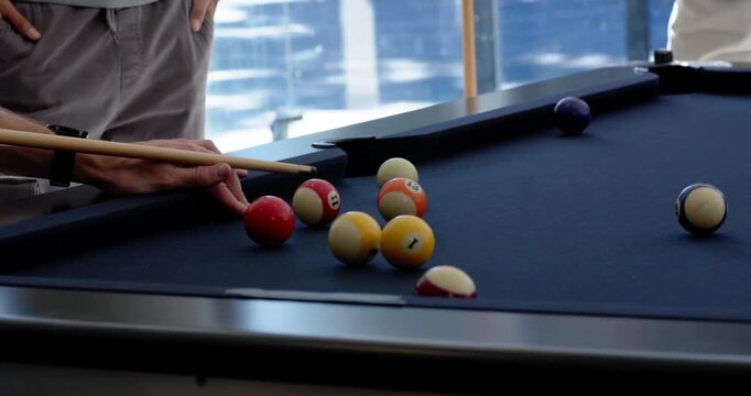 Diverse men watching shooter lining up and striking cue on pool table, rolling balls to sink