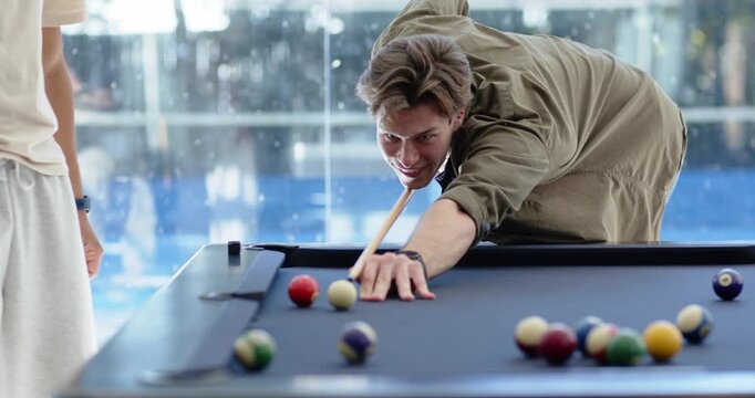 Male friends in lounge, shooter lining up cue on blue felt, striking balls hoping to score