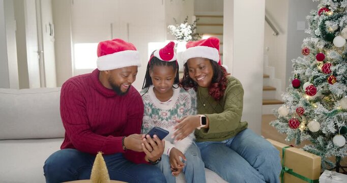 Family sitting on sofa at home dad raising phone taking selfies wearing Santa hats making memories