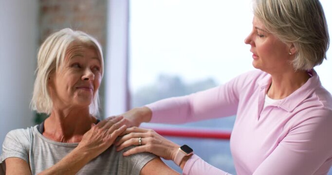 Senior woman and female PT starting shoulder exam, palpating, guiding arm in studio with smartwatch