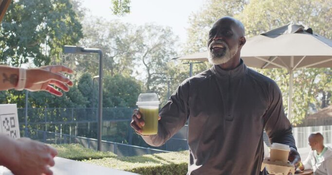 Senior man approaching cafe counter carrying green drink and two hot cups for server to arrange