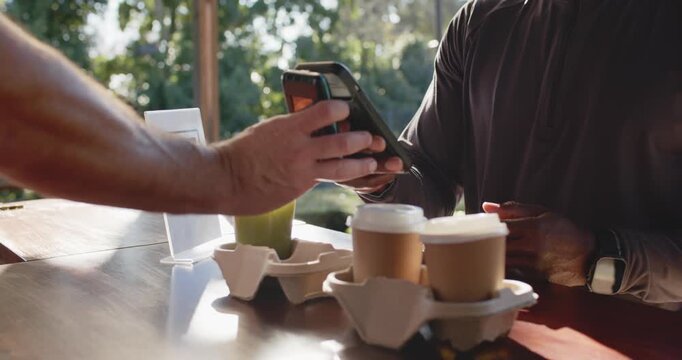African American man at outdoor counter taking payment while staff presenting phone, tapping reader