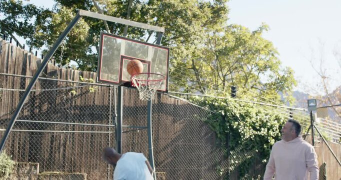 Diverse male pals starting play African American man dunking orange basketball scoring in backyard