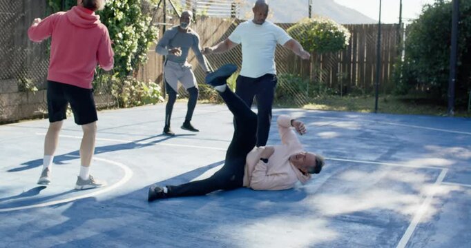 Male friends playing on blue court man in pink top losing balance contesting ball teammates pulling