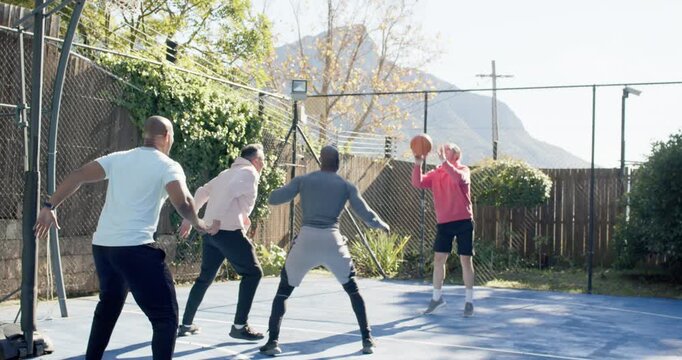 Diverse men dribbling as red-hoodie shooter shooting, trying score on fenced court, hoop scramble
