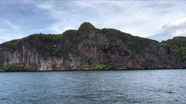 View of the dramatic limestone cliffs of Ko Phi Phi Lee rising from the turquoise sea under a bright sky in Ao Nang, Krabi, Thailand.