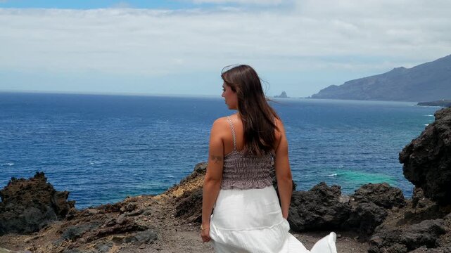 Joyful woman raising arms on volcanic island cliff