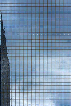 View of the modern glass facade of a skyscraper reflecting the cloudy sky with a geometric grid pattern in Calgary, Alberta, Canada.