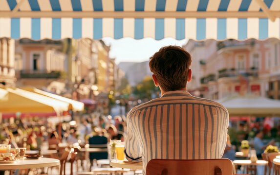 Man Sitting Alone at Outdoor Cafe Table Under Awning in Urban Street Scene