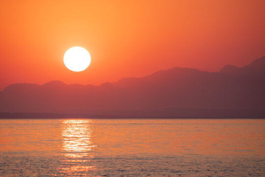 View of a vibrant sunset over the calm sea with silhouetted mountains in the background in Argassi, Greece.