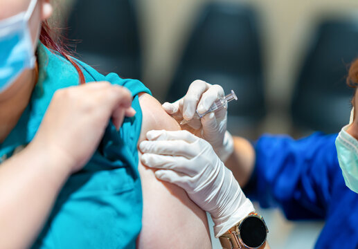 A healthcare worker injecting a dose of medication or flu shot into the upper arm of a patient wearing a face mask in a clinic setting.