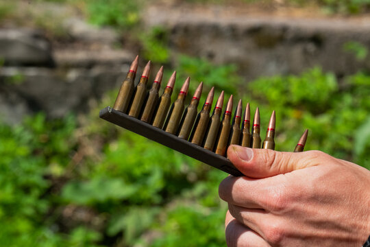 Hand holding vintage steel ammunition stripper clip with rifle bullets row target shooting view.
