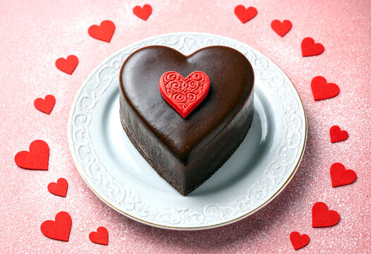 Delicious heartshaped chocolate cake with red heart decoration on a white plate surrounded by hearts