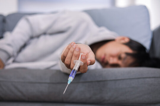 Man Unconscious on Sofa Holding Syringe After Drug Overdose, Focusing on Needle in His Head