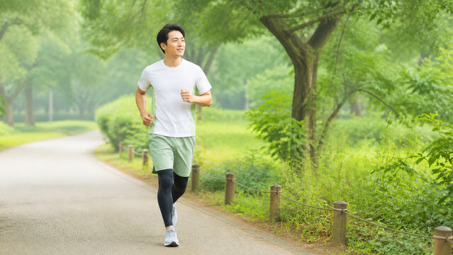 緑豊かな公園で無理なくジョギングを続ける成人日本人男性