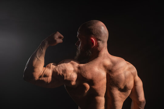 A male bodybuilder poses in shorts, showing off his back muscles.