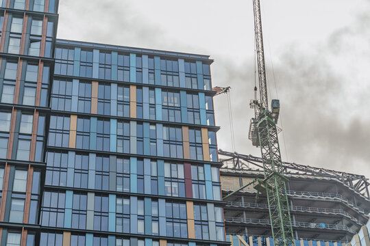 View of a modern high-rise building with a colorful glass facade and a construction crane under a cloudy sky in London, England, United Kingdom.