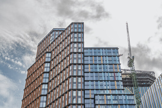 View of modern high-rise buildings with glass and metal facades and a construction crane against a cloudy sky in London, England, United Kingdom.