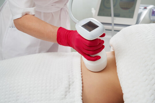 professional cosmetologist performing radiofrequency lifting procedure on the stomach of a woman
