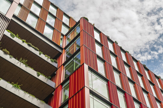 View of a modern office building with red vertical louvers, glass windows, and green balconies near Liverpool Street in London, England, United Kingdom.