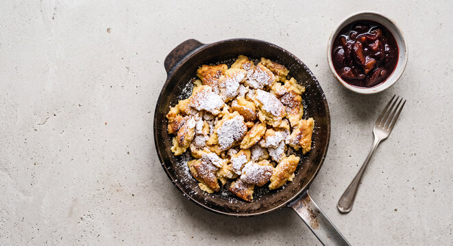 Traditional Austrian Kaiserschmarrn shredded pancake dusted with powdered sugar in cast iron pan with plum compote