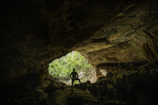 View of a hiker standing at the entrance of a limestone cave looking out into the lush green forest of the Reserve speciale d'Ankarana in Diana, Madagascar.