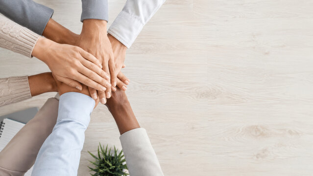 Top view of diverse hands join together in unity showing teamwork and support on light wooden table background
