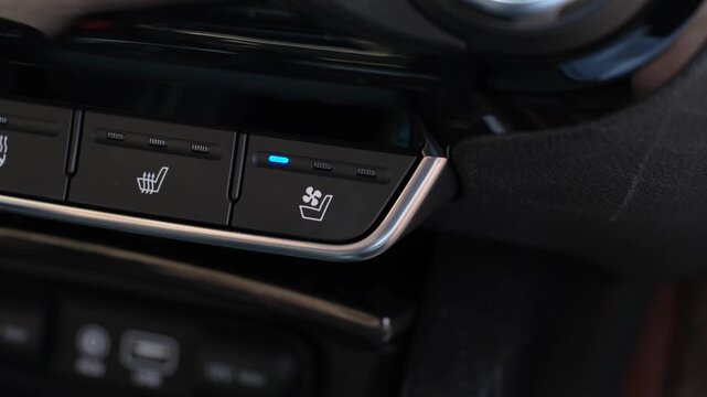 A close-up of a man's finger pressing button for air-conditioned car seats.