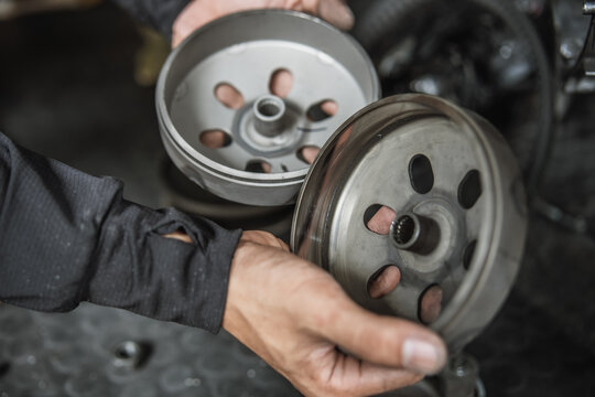 Mechanic hands holding motorcycle clutch bells for inspection during CVT transmission repair
