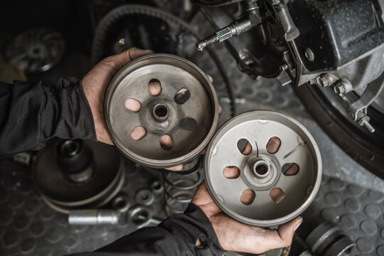 Mechanic hands holding motorcycle clutch bells for inspection during CVT transmission repair