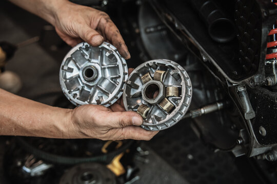 Mechanic hands holding motorcycle CVT variator pulley and roller weights during transmission inspection