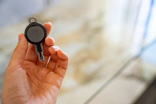 Hand holding an RFID key fob with electronic access chip inside a modern apartment. Concept of smart access control, keyless entry and residential security.