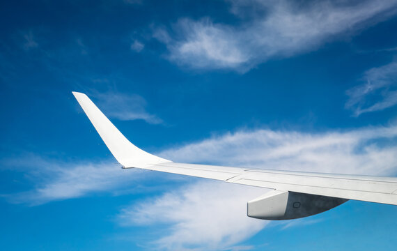 Commercial airplane wing seen from passenger window while flying above clouds under clear blue sky. Modern aviation, international flight, travel experience and tourism concept. Global tourism.