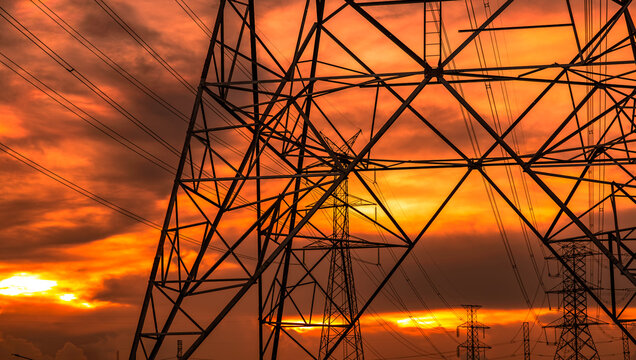 Steel lattice electricity transmission towers and overhead power lines during golden sunset representing electrical infrastructure, sustainable energy supply, utility engineering and modern power grid