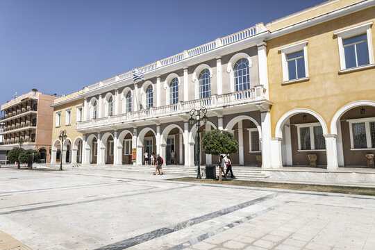 Zakinthos, Greece - 01 August 2026: View of the neoclassical Town Hall in Solomos Square, featuring arched colonnades, large windows, and people walking on the marble square.