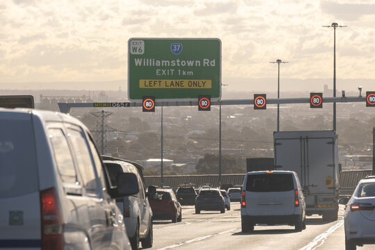 Overhead green highway signage of Williamstown Road exit&nbsp;on the West Gate Freeway with heavy traffic with a hazy background of western suburbs of Melbourne Australia.