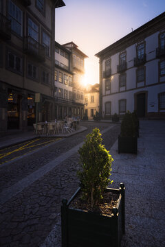 Guimaraes, Braga, Portugal - 10 August 2026: View of a historic street in Guimaraes with cobblestone pavement, traditional buildings, and sunlight filtering through the buildings at sunset.
